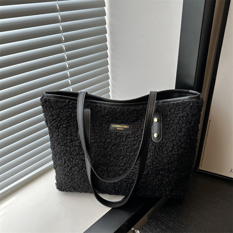 Black textured handbag with a visible brand logo on a surface near a window.