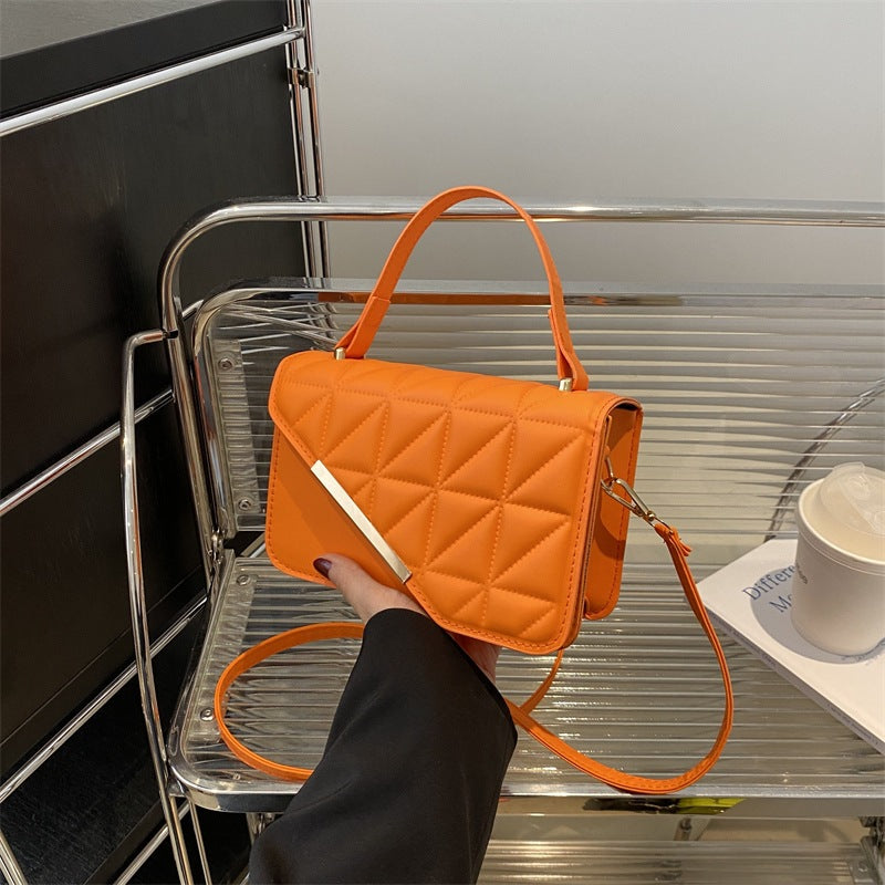 Orange quilted handbag held by a person on a metal shelf.