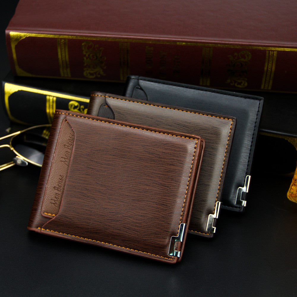 Three leather wallets in brown, black, and gray on a dark surface with books and glasses in the background.